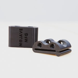 May include: Two black plastic components. One is rectangular with "MOJAVE MFG" printed on the side. The other is a curved shape with three holes. Both are on a white background.