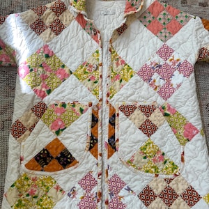 May include: A quilted jacket featuring a patchwork design of white fabric squares alternating with colorful floral and geometric patterned squares. The jacket has a collar, a front button closure, and two large patch pockets on the front.