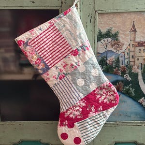 May include: A quilted Christmas stocking featuring a patchwork design of various fabrics, including red and white stripes, pink floral patterns, light blue polka dots, and blue and white pinstripes, with a fabric loop at the top for hanging.