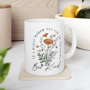 May include: White ceramic mug with a floral design and the text "In a world where you can be anything, Bee Kind".