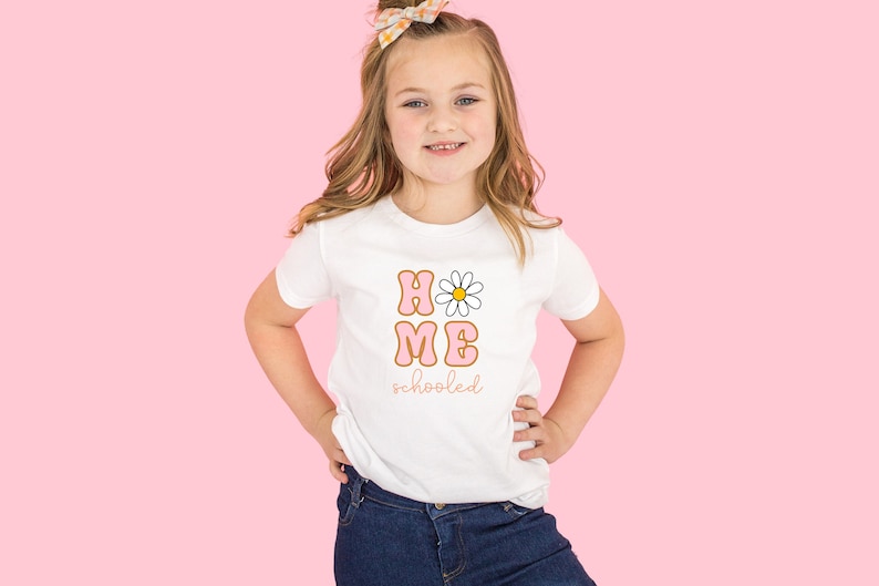 K&ouml;nnte beinhalten: Ein wei&szlig;es T-Shirt mit einer pinkfarbenen und orangenen Grafik, auf der "HOME" mit einer G&auml;nsebl&uuml;mchen und "schooled" darunter steht.