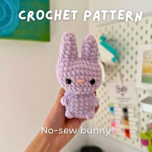 Puede incluir: Un conejito de ganchillo lavanda con ojos negros y nariz rosa. El texto "CROCHET PATTERN" está encima del conejito, y "No-sew bunny" debajo. El conejito está hecho de un hilo suave y texturizado. Un artículo de artesanía hecho a mano.
