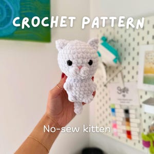 Puede incluir: Un patrón de ganchillo de gatito sin costuras. El pequeño gatito blanco tiene ojos negros y una nariz rosa. El texto "CROCHET PATTERN" está en la parte superior y "No-sew kitten" en la inferior.