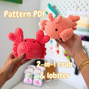 Puede incluir: Dos peluches de crochet de cangrejo y langosta en tonos rojos y melocotón. El texto "Pattern PDF" y "2-en-1 cangrejo y langosta" son visibles. Los peluches tienen ojos negros.