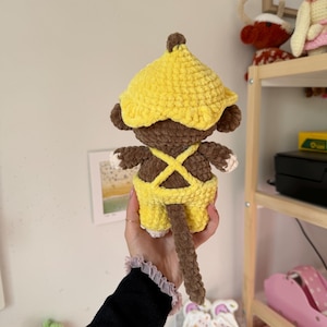 May include: A handmade crochet monkey doll, featuring a yellow hat and overalls. The monkey has brown fur, white hands and feet, and a long brown tail. The doll is a soft, plush toy.