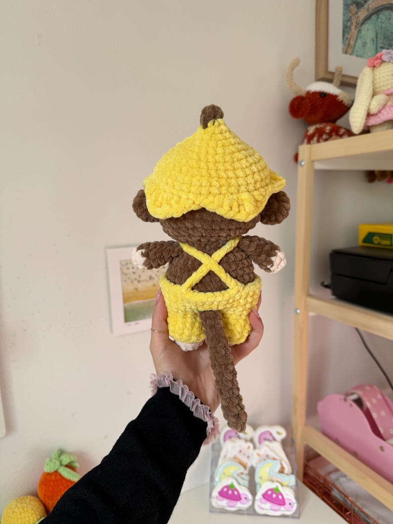 May include: A handmade crochet monkey doll, featuring a yellow hat and overalls. The monkey has brown fur, white hands and feet, and a long brown tail. The doll is a soft, plush toy.