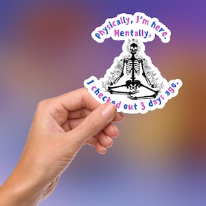 May include: A white sticker with a black skeleton sitting in a lotus position with flowers around it. The text on the sticker reads "Physically, I'm here. Mentally, I checked out 3 days ago."
