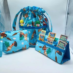 May include: A set of three matching blue fabric items featuring a tropical print with a woman holding a paddle. The set includes a drawstring bag, a zippered pouch, and a stand-up organizer. The drawstring bag has a blue rope handle.