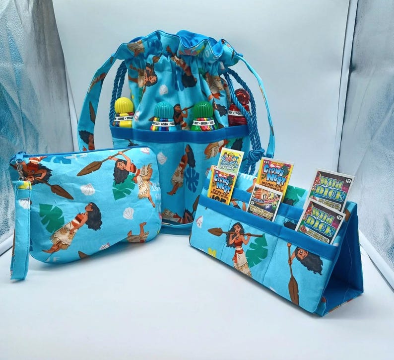 May include: A set of three matching blue fabric items featuring a tropical print with a woman holding a paddle. The set includes a drawstring bag, a zippered pouch, and a stand-up organizer. The drawstring bag has a blue rope handle.