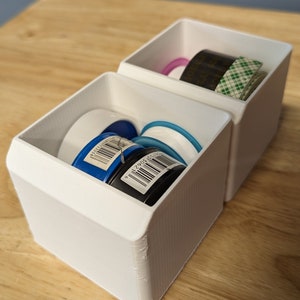 May include: Two white plastic containers with lids, one containing rolls of blue, black, and white tape, and the other containing a roll of green and black tape.