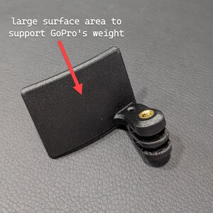 May include: Black GoPro mount with a large surface area for weight support. The mount has a rectangular base and a three-prong connector with a brass-coloured screw.