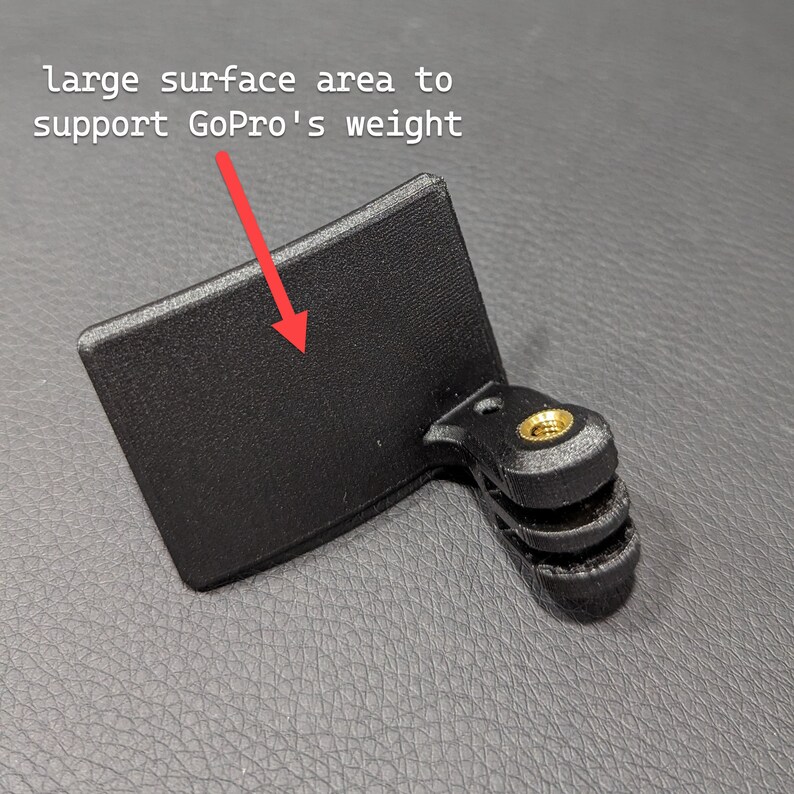 May include: Black GoPro mount with a large surface area for weight support. The mount has a rectangular base and a three-prong connector with a brass-coloured screw.
