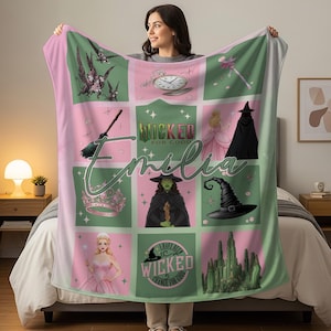 Peut inclure: Une couverture rose et verte personnalisée avec des images de la comédie musicale "Wicked". Le design comprend une horloge, un chapeau de sorcière, une couronne et le texte "Wicked for Good" et "Emilia".