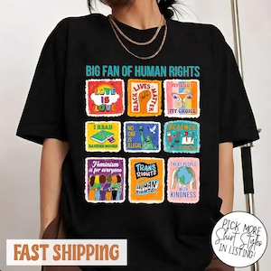 Op de afbeelding: Zwart T-shirt met de tekst "BIG FAN OF HUMAN RIGHTS" en diverse kleurrijke vierkante afbeeldingen. De afbeeldingen bevatten zinnen als "Love is Love" en "Treat People with Kindness".