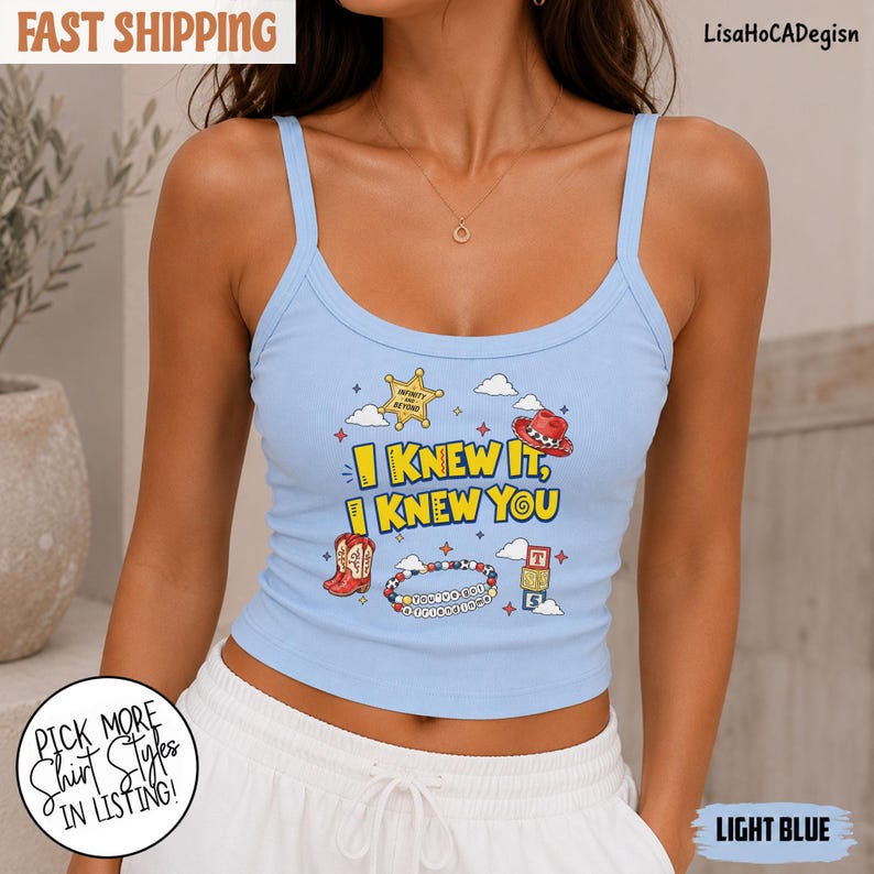 May include: A light blue ribbed tank top featuring a graphic print with the text "I KNEW IT, I KNEW YOU" in yellow, surrounded by illustrations of a sheriff badge, a cowboy hat, red cowboy boots, a beaded bracelet, and alphabet blocks.