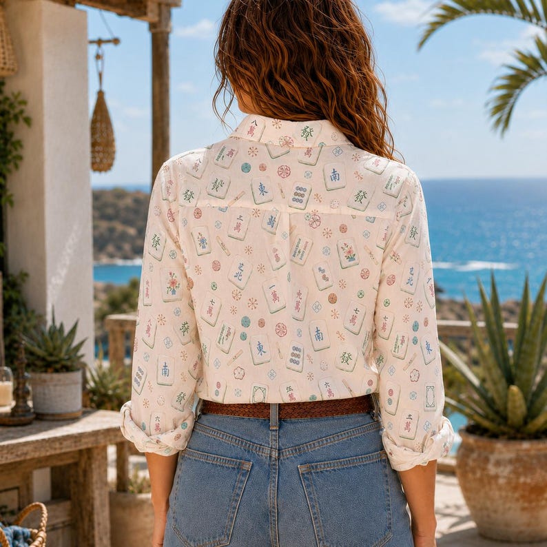 Puede incluir: Una camisa de manga larga abotonada en color blanco roto con un estampado integral de fichas de Mahjong coloridas y peque&ntilde;os motivos florales circulares. La camisa tiene un cuello cl&aacute;sico, pu&ntilde;os abotonados y est&aacute; metida en vaqueros azules.