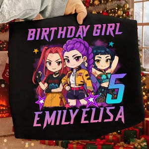 Peut inclure: Sac fourre-tout noir avec une illustration de style anime de trois filles. Le texte "BIRTHDAY GIRL" et "EMILY ELISA 5" sont en violet et bleu. Les filles ont les cheveux rouges, violets et bleus.