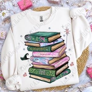 May include: White crew neck sweatshirt with a design of stacked books in green and pink. The books have titles such as "Popular" and "Delving Gravity." A witch's hat and stars are also included. A comfortable, casual style.