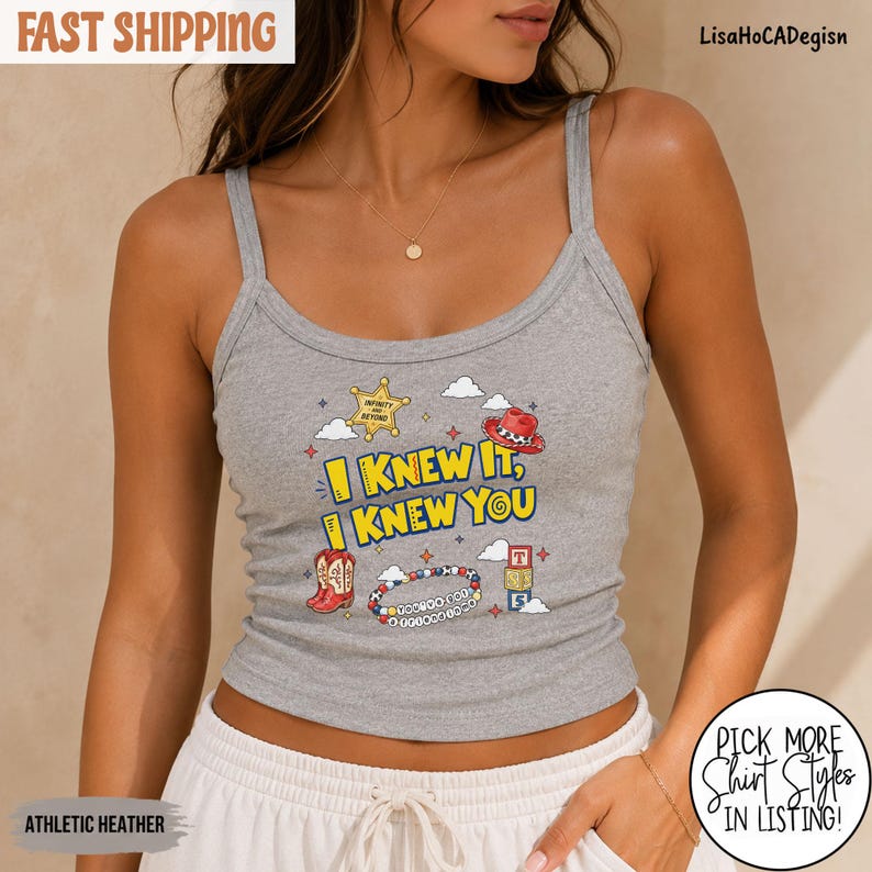 May include: A heather gray tank top featuring a graphic print with the text I KNEW IT, I KNEW YOU. The design includes a yellow sheriff star, a red cowboy hat, a red cowboy boot, a colorful beaded bracelet, and a stack of alphabet blocks.