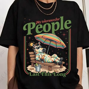 May include: Black t-shirt with a colorful graphic of a zebra relaxing on a beach chair under a rainbow umbrella. The text reads "My tolerance for People Last This Long."