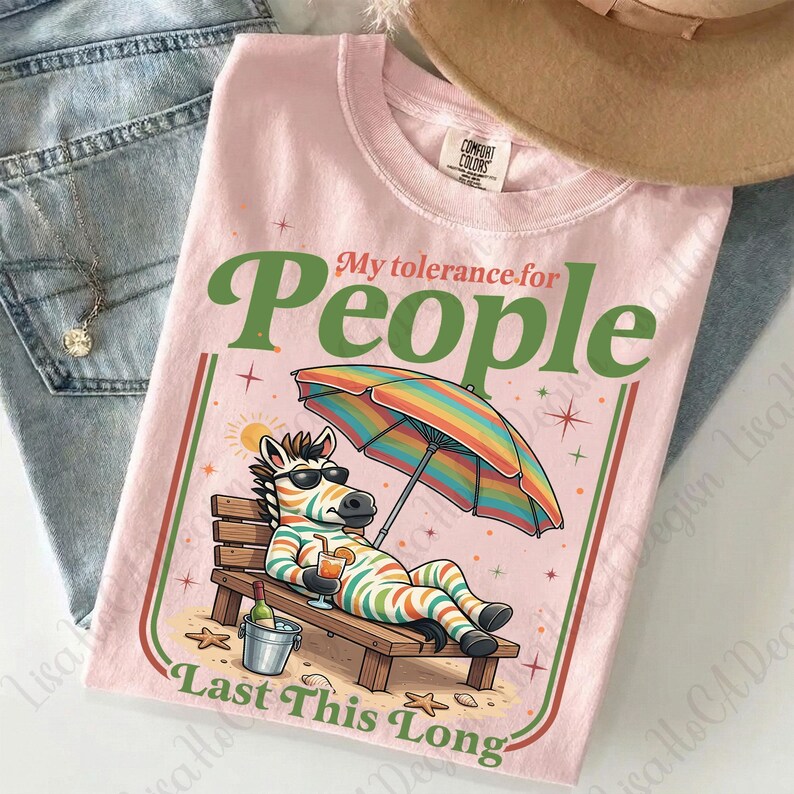 May include: Pink t-shirt with the text "My tolerance for People Last This Long". The shirt features a cartoon zebra relaxing on a beach chair under a rainbow umbrella, holding a drink. A bucket with a bottle of wine is next to the chair.