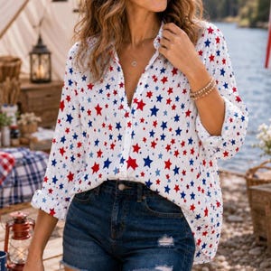 May include: White button-down shirt with a pattern of red and blue stars. The long-sleeved shirt is paired with denim shorts. The shirt has a classic collar and buttoned cuffs. The overall style is casual and patriotic.