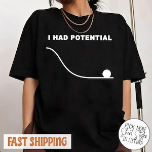Puede incluir: Camiseta negra con el texto blanco "I HAD POTENTIAL" sobre un gráfico blanco de una bola rodando por una línea curva. La camiseta es de estilo casual.