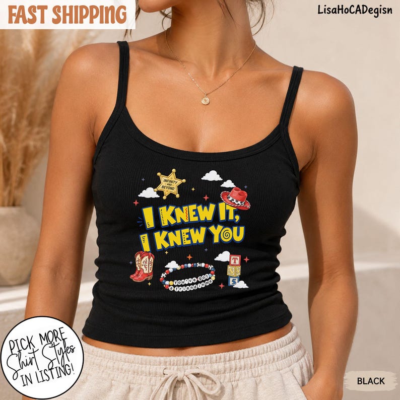 May include: A black ribbed tank top featuring a graphic print with the yellow text I KNEW IT, I KNEW YOU, a gold sheriff star, a red cowboy hat, a beaded bracelet, and stacked alphabet blocks, all surrounded by small white clouds and stars.