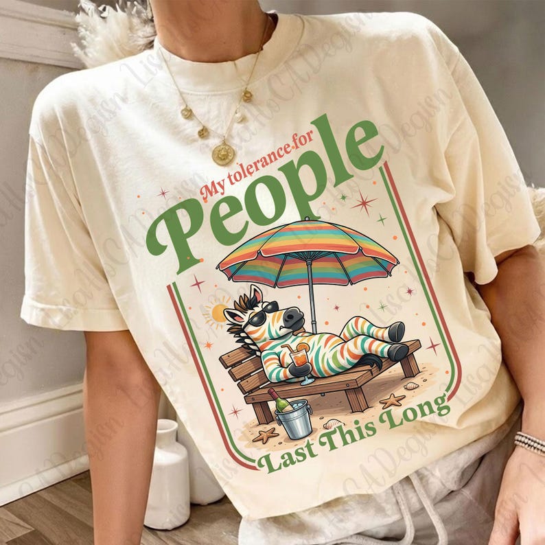 May include: Cream-colored t-shirt featuring a zebra relaxing on a beach chair under a rainbow umbrella. The shirt has the text "My tolerance for People Last This Long" in green and red. A fun, casual tee.