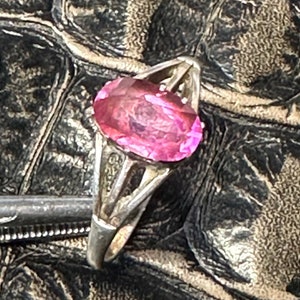 May include: A silver ring featuring a pink oval-shaped gemstone. The ring has a delicate, intricate design.