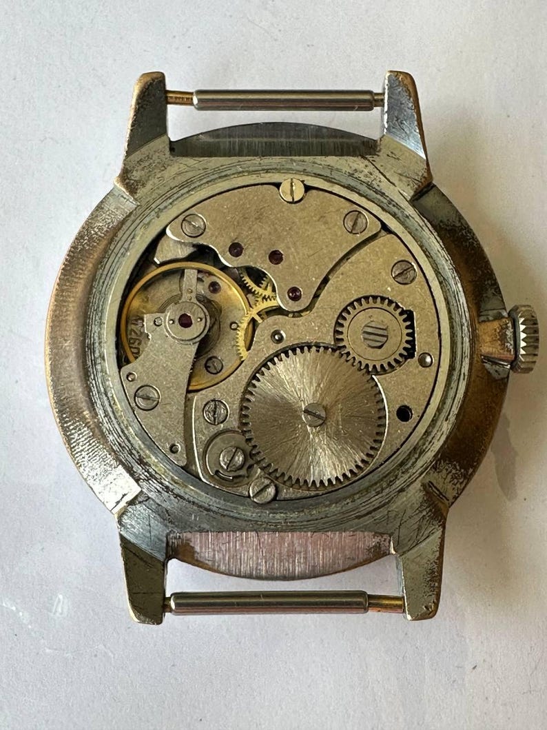May include: The back of a silver wristwatch with a round, silver case and a visible mechanical movement. The watch has a brown leather strap with a silver buckle.