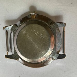 May include: The back of a silver wristwatch with a round case and a metal band. The watch face has a number "607425" printed on it.
