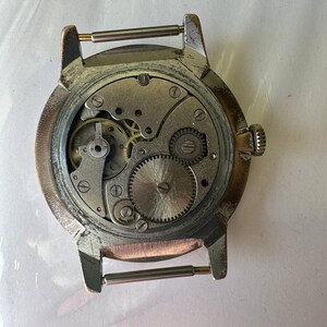 May include: The back of a silver wristwatch with a round face and a metal band. The watch face is open, revealing the inner workings of the watch.