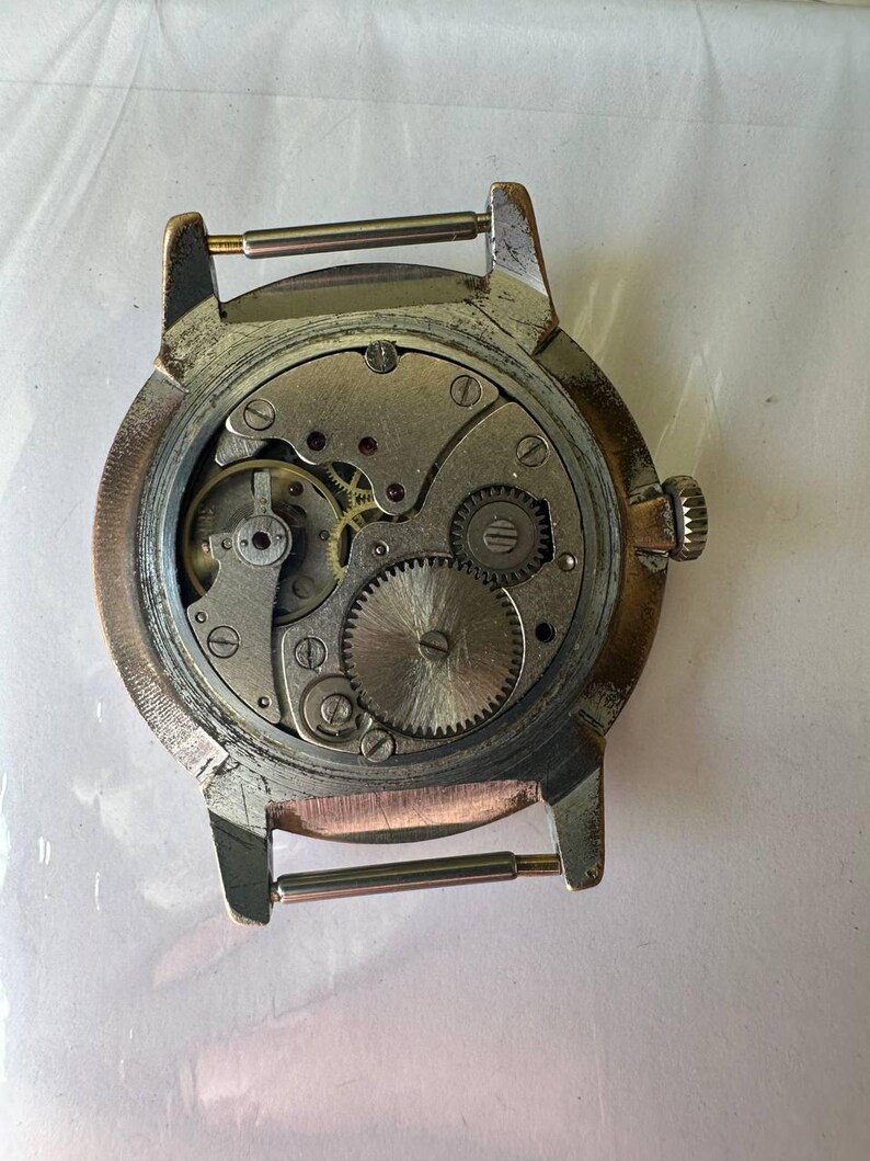 May include: The back of a silver wristwatch with a round face and a metal band. The watch face is open, revealing the inner workings of the watch.
