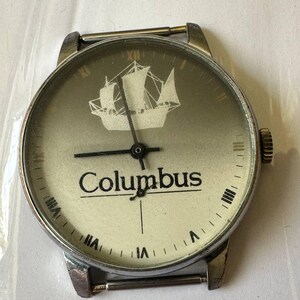 May include: A silver wristwatch with a white face and black hands. The face has a ship design and the word "Columbus" printed on it.