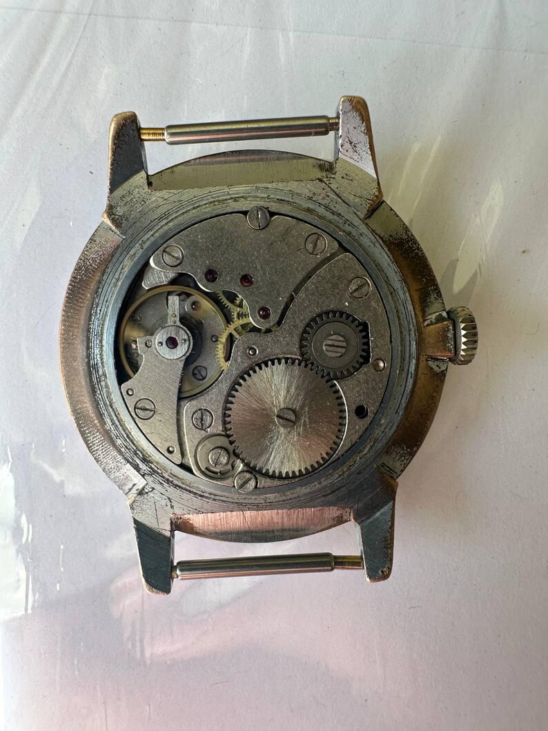 May include: The back of a silver wristwatch with a visible mechanical movement. The watch has a round case and a metal band.