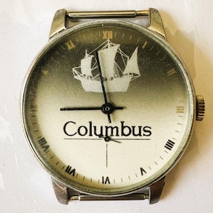May include: A vintage silver wristwatch with a white face and black hands. The face features a ship silhouette and the word "Columbus".