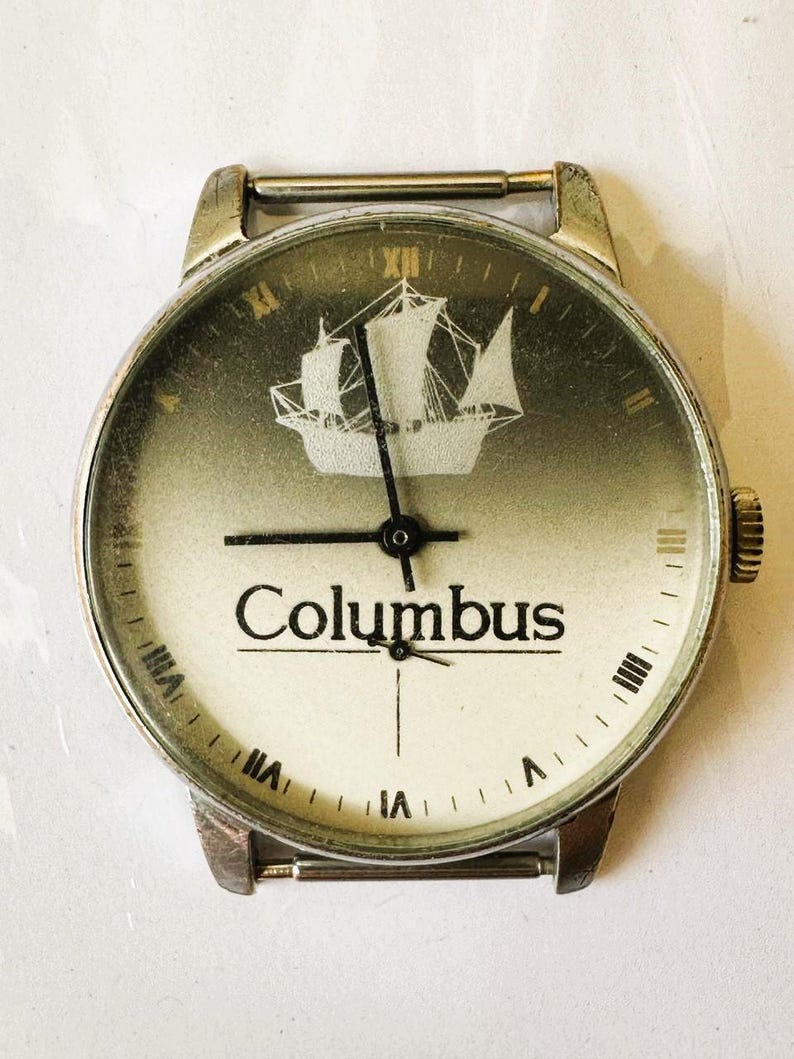 May include: A vintage silver wristwatch with a white face and black hands. The face features a ship silhouette and the word "Columbus".