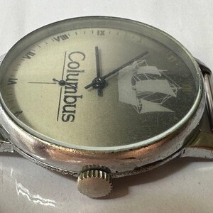 May include: A silver wristwatch with a white face and black hands. The face has the word "Columbus" printed on it and a ship design. The watch has a silver band.