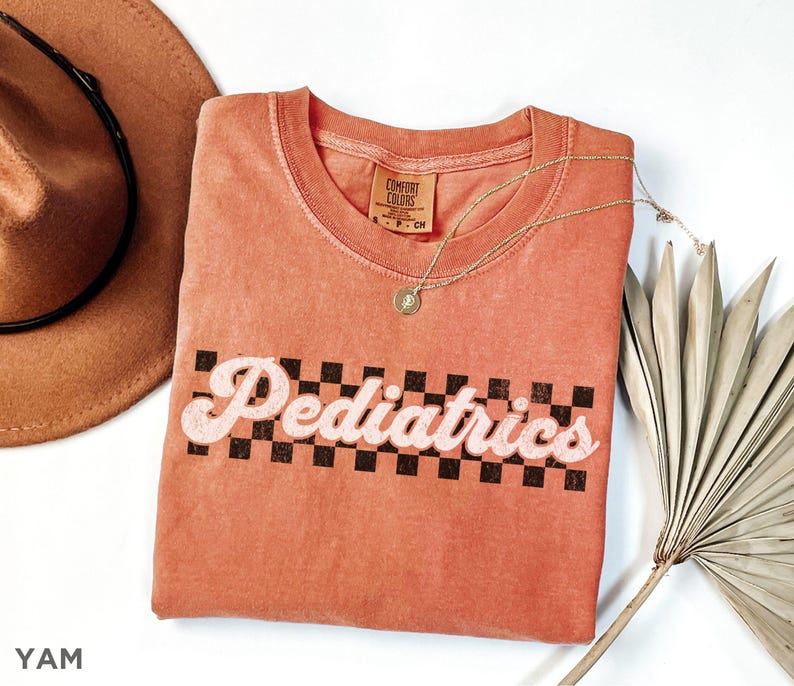 May include: A coral coloured t-shirt with a black and white chequered design and the text "Pediatrics" in a retro font.
