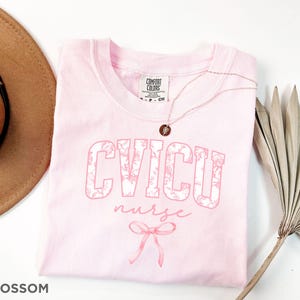 May include: Pink t-shirt with a floral design that says "CVICU nurse" with a pink bow.