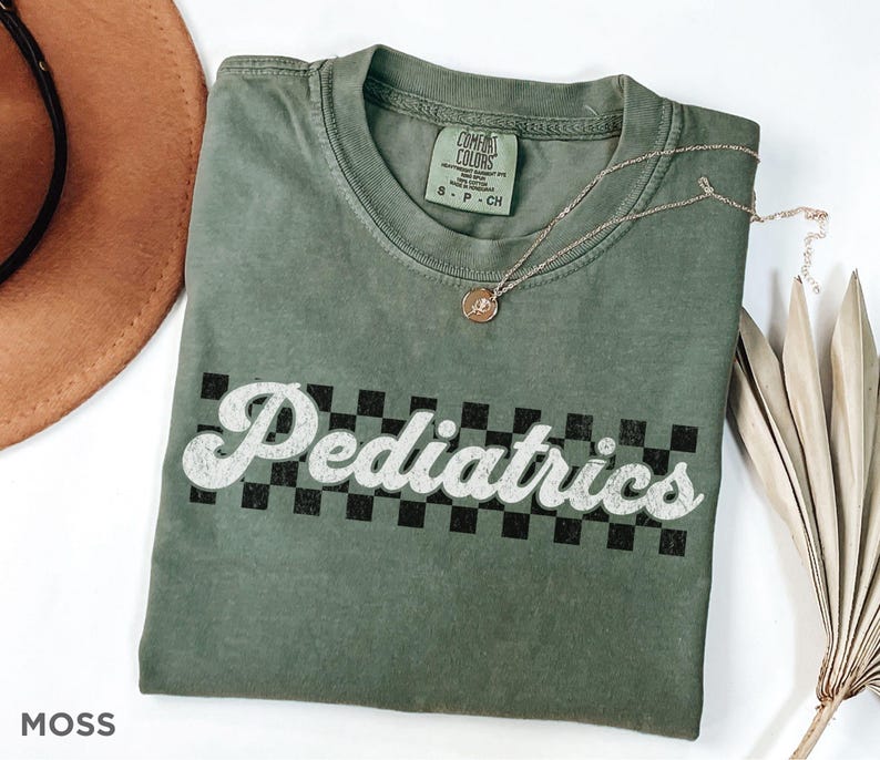 May include: A green t-shirt with a white graphic that says "Pediatrics" in a retro font with a black and white checkered pattern behind the text.