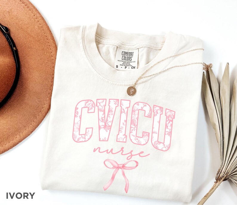 May include: Ivory t-shirt with a pink floral design that says "CVICU nurse" with a pink bow underneath.