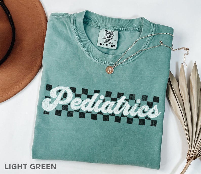May include: Light green t-shirt with a white checkered pattern and the text "Pediatrics" in a retro font.