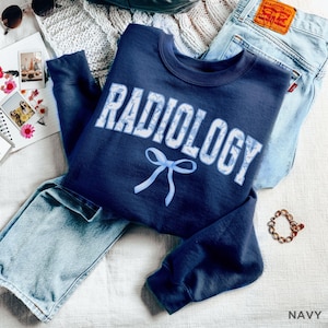 May include: Navy blue sweatshirt with a white and blue floral design that says "RADIOLOGY" with a blue bow underneath.