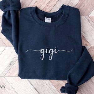 May include: Navy blue sweatshirt with the word "gigi" written in white cursive script.