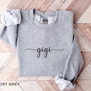 May include: A gray sweatshirt with the word "gigi" written in cursive on the front. The sweatshirt is made of a soft, comfortable material and is perfect for everyday wear.