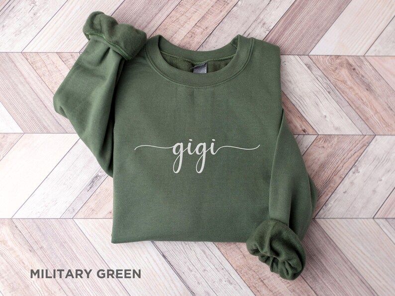 May include: A military green sweatshirt with the word "gigi" written in white cursive script.