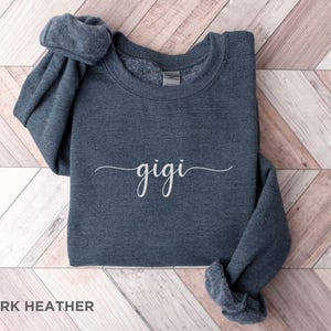 May include: Dark heather grey sweatshirt with the word "gigi" written in white cursive script.