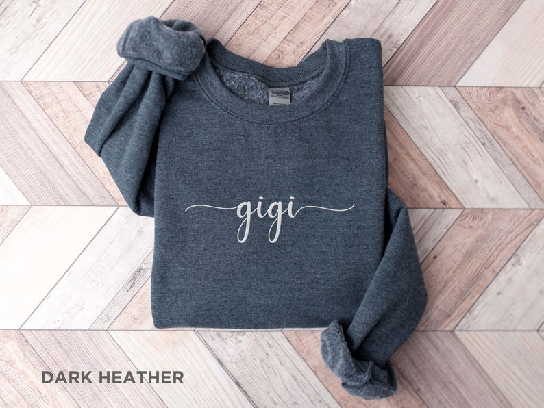 May include: Dark heather grey sweatshirt with the word "gigi" written in white cursive script.